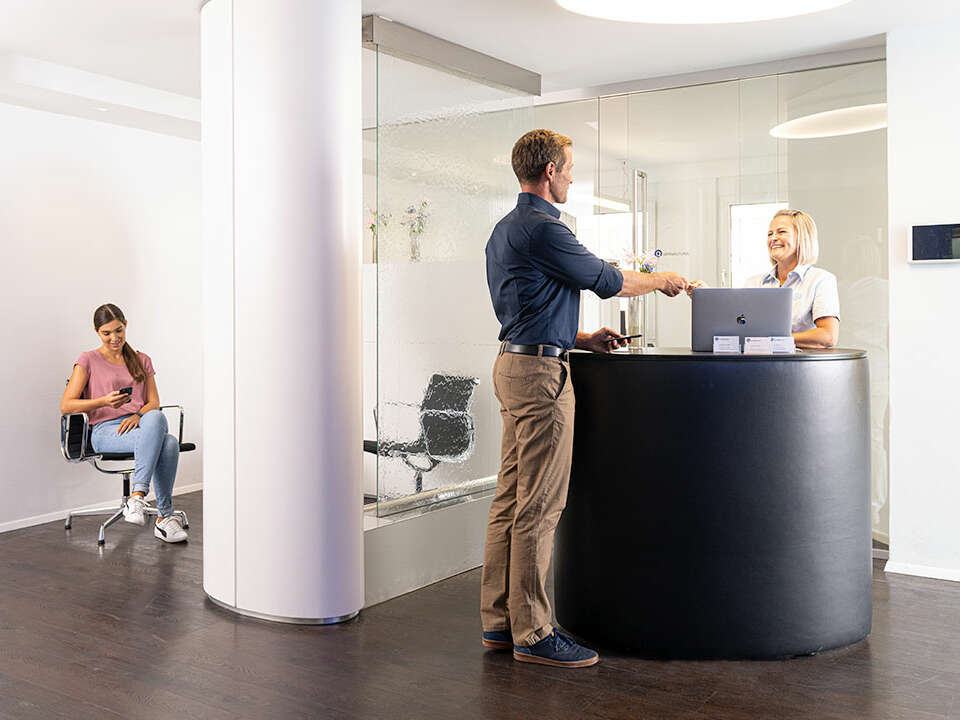 Two dental assistants discuss a customer appointment at the reception desk of the practice.